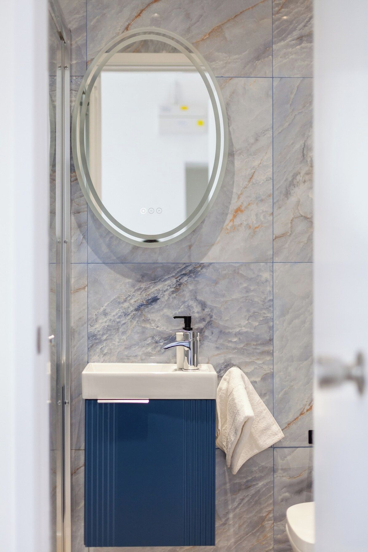 A bathroom with a marble wall, a round mirror, a sink with a faucet, and a towel hanging on the wall.