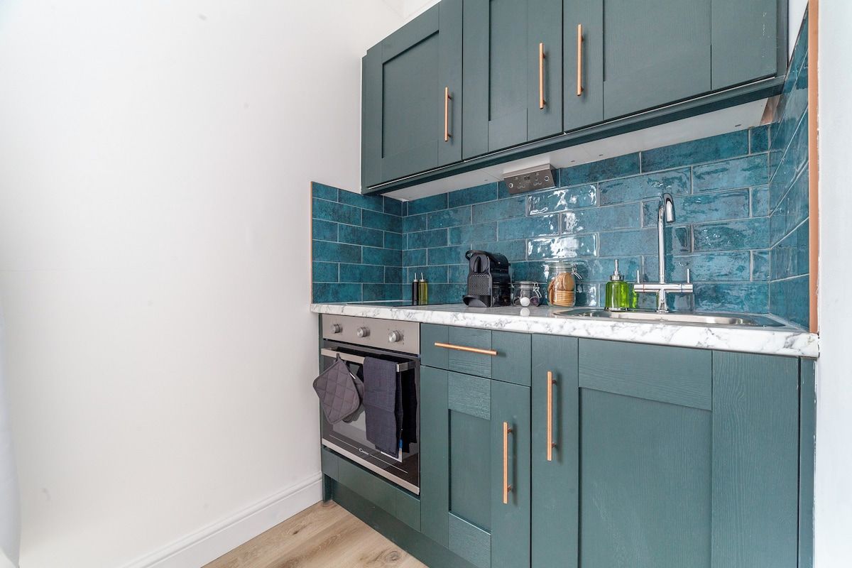 Una cucina compatta con mobili color acquamarina, forno integrato e un piano di lavoro in marmo.