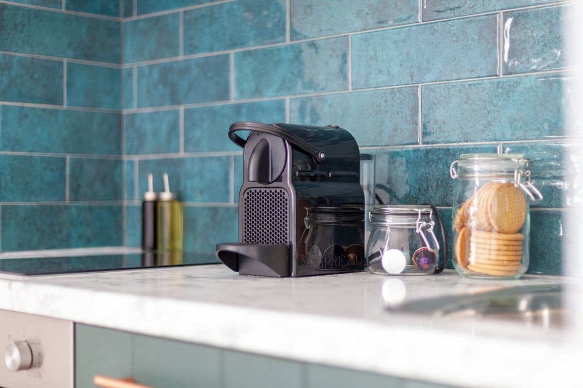 A kitchen counter with a coffee maker, a glass jar with cookies, and a bottle of olive oil.