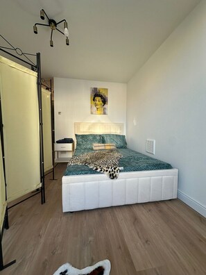 A bedroom with a bed, a headboard, a wall-mounted picture, and a ceiling light fixture. - Gorgeous Studio Flat, Finsbury Park (Greater London)