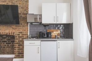 A compact kitchen with white cabinets, a brick wall, a flat-screen TV, and a coffee maker. - Fabulous Studio Flat Kilburn - Central Location (Greater London)