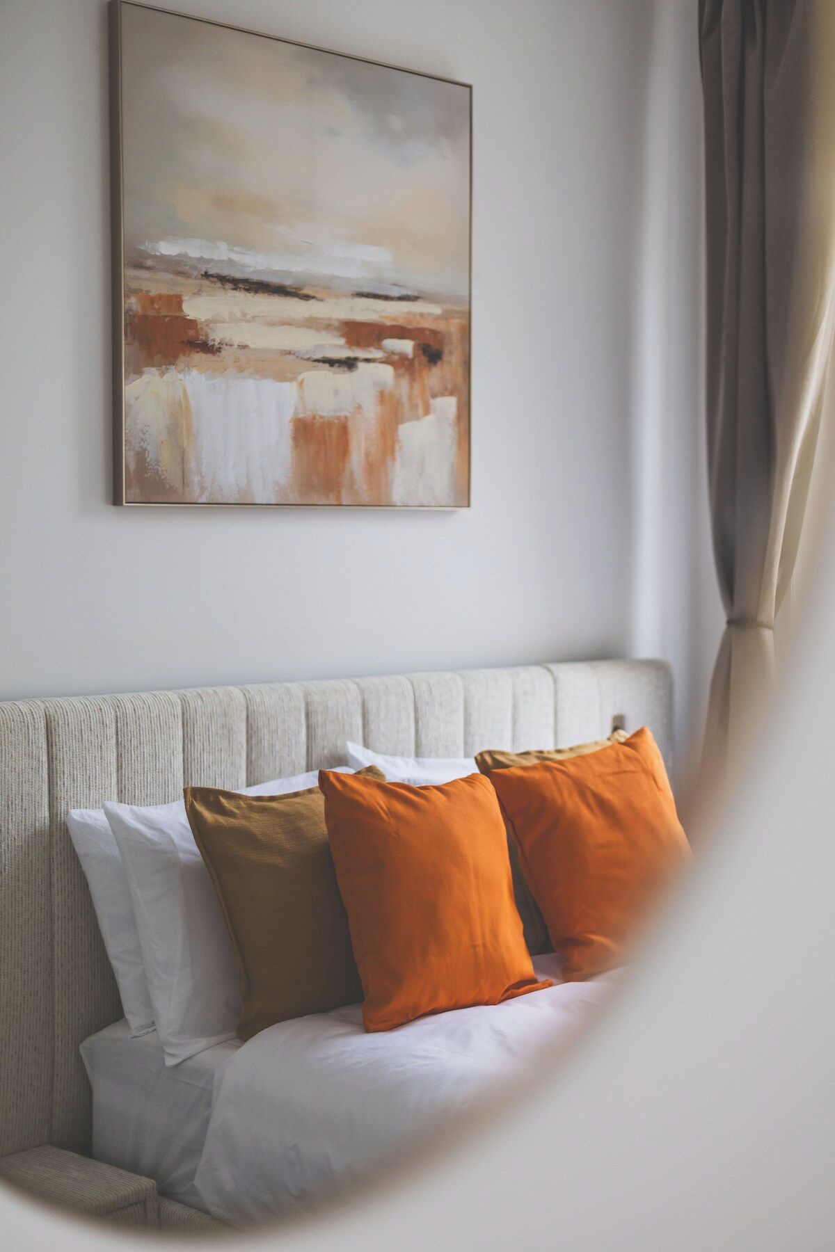 A room with a sofa, two pillows, a painting on the wall, and a curtain.