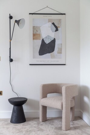 Ein Zimmer mit einem gerahmten abstrakten Kunstwerk mit dem Titel 'Paper Cuts' aus der 'The Abstract Art Collection, Stockholm 2020', einer schwarzen Stehlampe, einem runden schwarzen Beistelltisch und einem beige gestreiftem Sessel.