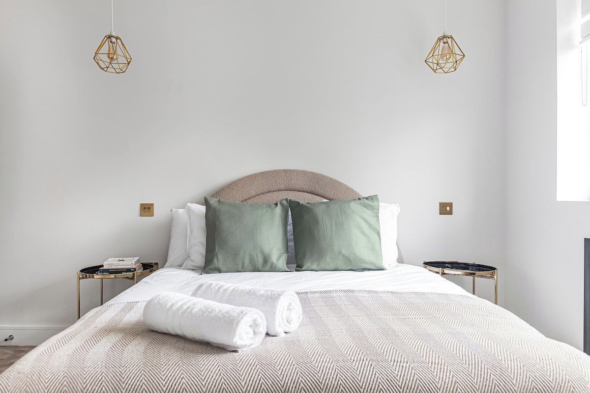 A neatly made bed with a white comforter and two pillows, a round headboard, and two bedside tables with lamps.
