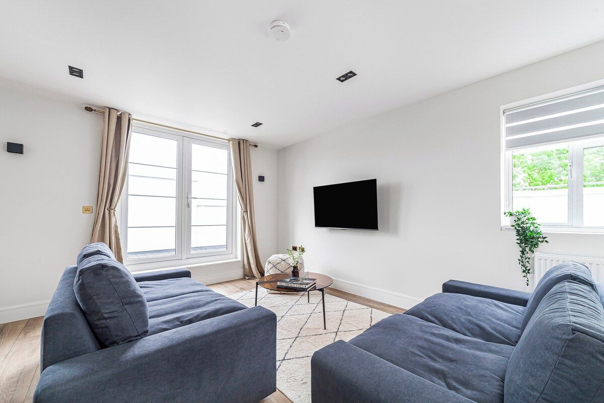 Un salon moderne avec deux canapés gris, un téléviseur à écran plat et une grande fenêtre avec des rideaux.