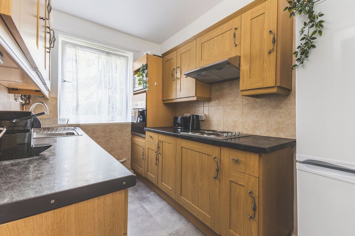 A modern kitchen with wooden cabinets, a black countertop, and a stainless steel range hood.