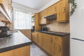 A modern kitchen with wooden cabinets, a black countertop, and a stainless steel range hood. - Tower Bridge 2 Bedroom Flat | Sleeps 5 | Great (Greater London)