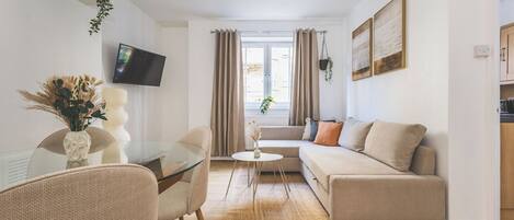 Un salon moderne avec un canapé, une table à manger en verre et un téléviseur fixé au mur.