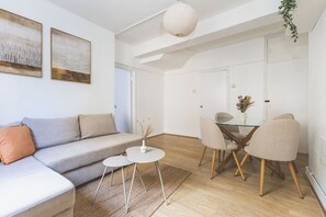 A modern living room with a sofa, coffee table, and dining area with chairs. - Tower Bridge 2 Bedroom Flat | Sleeps 5 | Great (Greater London)