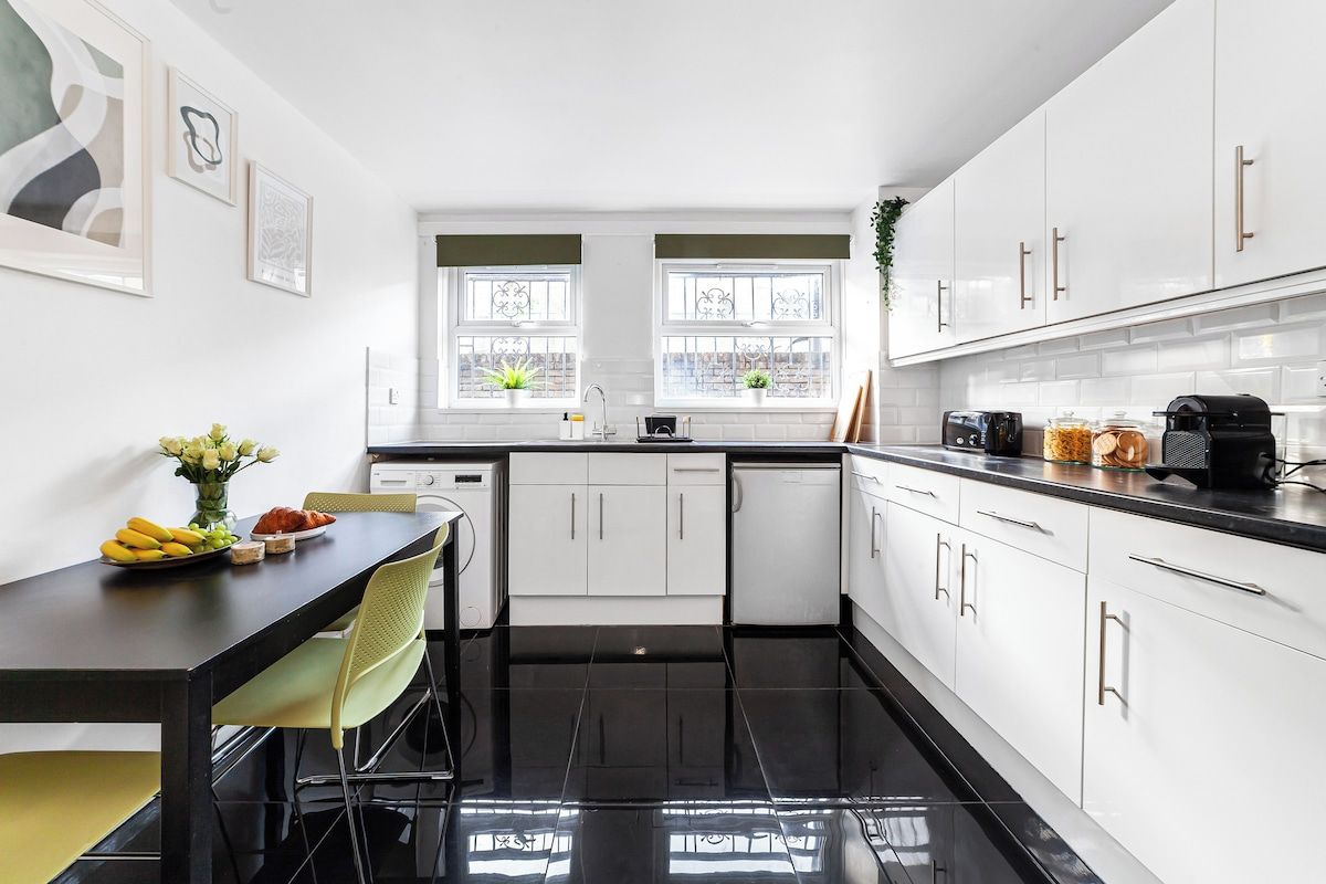 A modern kitchen with white cabinets, a black countertop, and a dining area with a table and chairs.