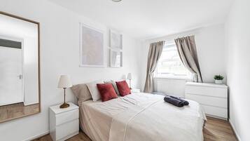 Quarto com cama, mesas de cabeceira, janela com cortinas e decoração na parede.