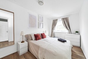 Quarto com cama, mesas de cabeceira, janela com cortinas e decoração na parede.