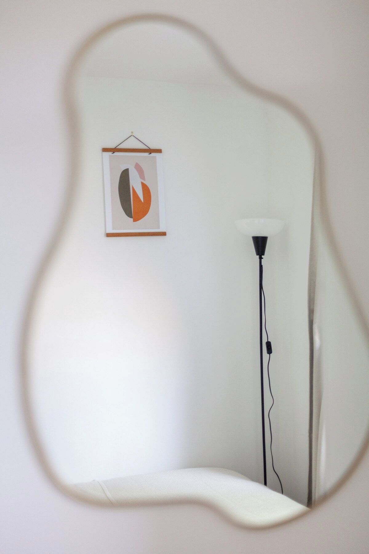A room with a floor lamp, a framed abstract artwork, and a mirror reflecting the room's corner.
