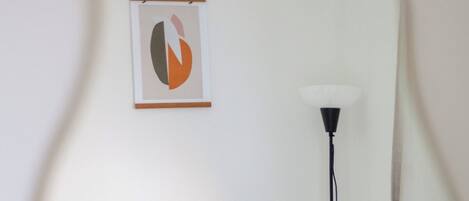 A room with a floor lamp, a framed abstract artwork, and a mirror reflecting the room's corner.