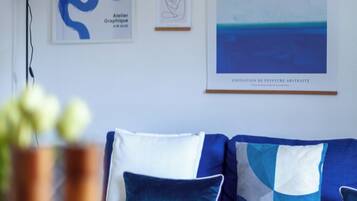 A modern living room with a blue sofa, a framed abstract painting, and a hanging light fixture.