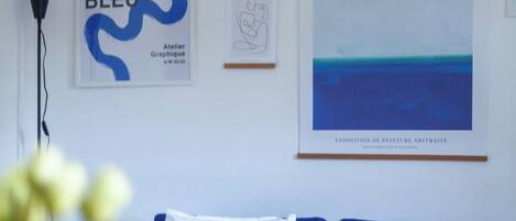 A modern living room with a blue sofa, a framed abstract painting, and a hanging light fixture.