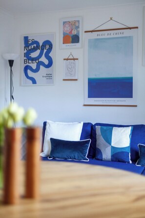 Uma sala de estar moderna com um sofá azul, uma pintura abstrata emoldurada e um lustre.