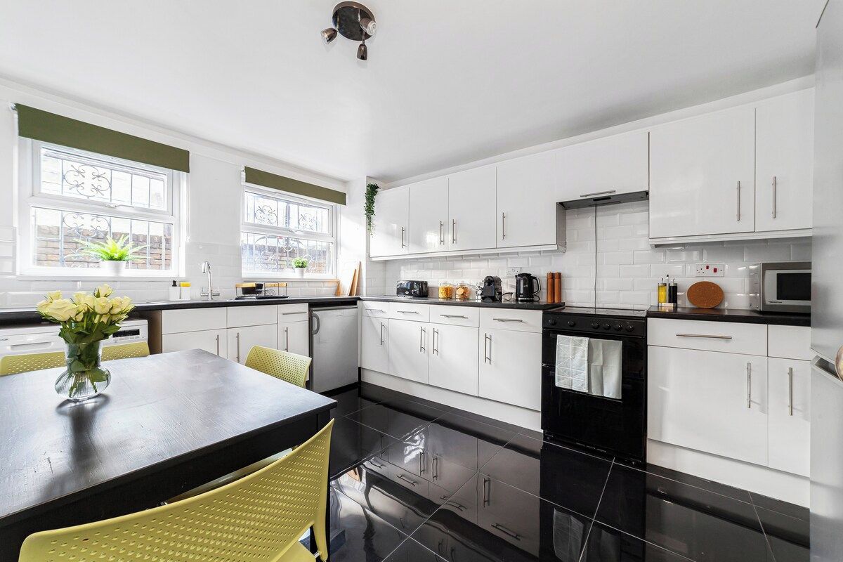 A modern kitchen with white cabinets, a black countertop, and a dining area with yellow chairs.