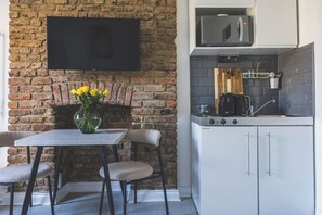A kitchen with a flat-screen TV mounted on a brick wall, a coffee machine, and a microwave. - Stylish & Petit Studio flat Kilburn (Greater London)