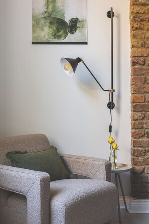 A room with a sofa, a floor lamp, a painting, and a brick wall. - Stylish & Petit Studio flat Kilburn (Greater London)