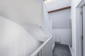 A narrow, white-walled hallway with a wooden beam ceiling, a white door, and a radiator on the wall. - New Spacious 3 bed flat Duplex, Whitechapel (Greater London)