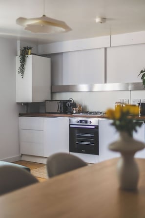 A modern kitchen with white cabinets, a built-in oven, and a dining area with a wooden table. - New Spacious 3 bed flat Duplex, Whitechapel (Greater London)
