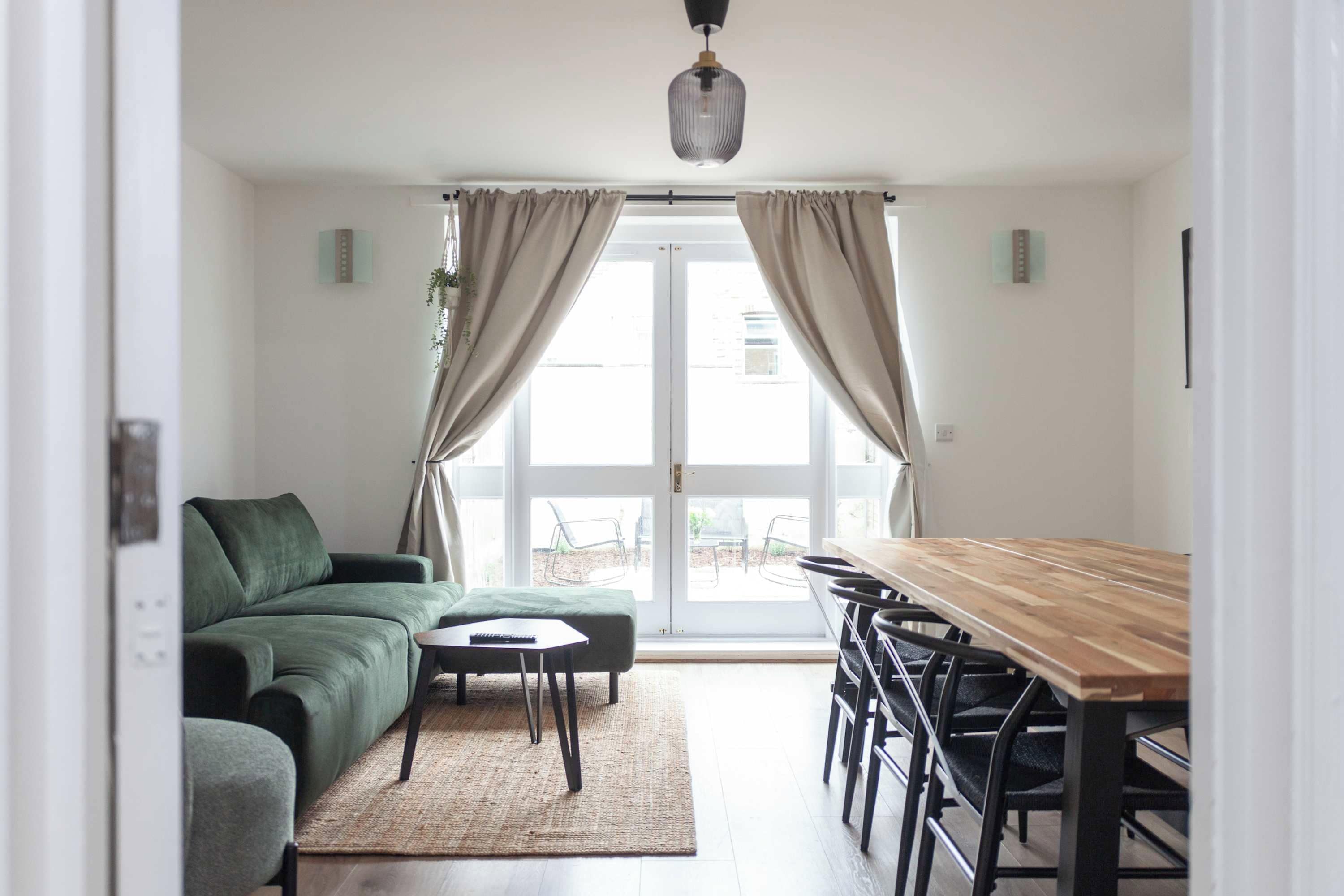 Un salon moderne avec un canapé vert, une petite table et une table à manger en bois, accompagnée de chaises.