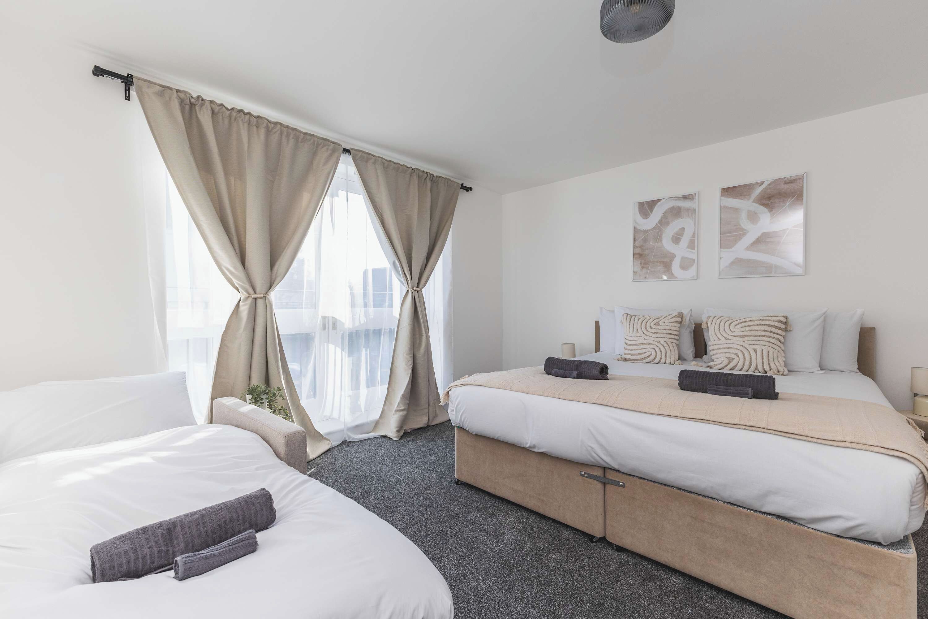 Ein Hotelzimmer mit zwei Betten, einem großen Fenster mit Vorhängen, Blick auf die Stadt und abstrakter Wandkunst.