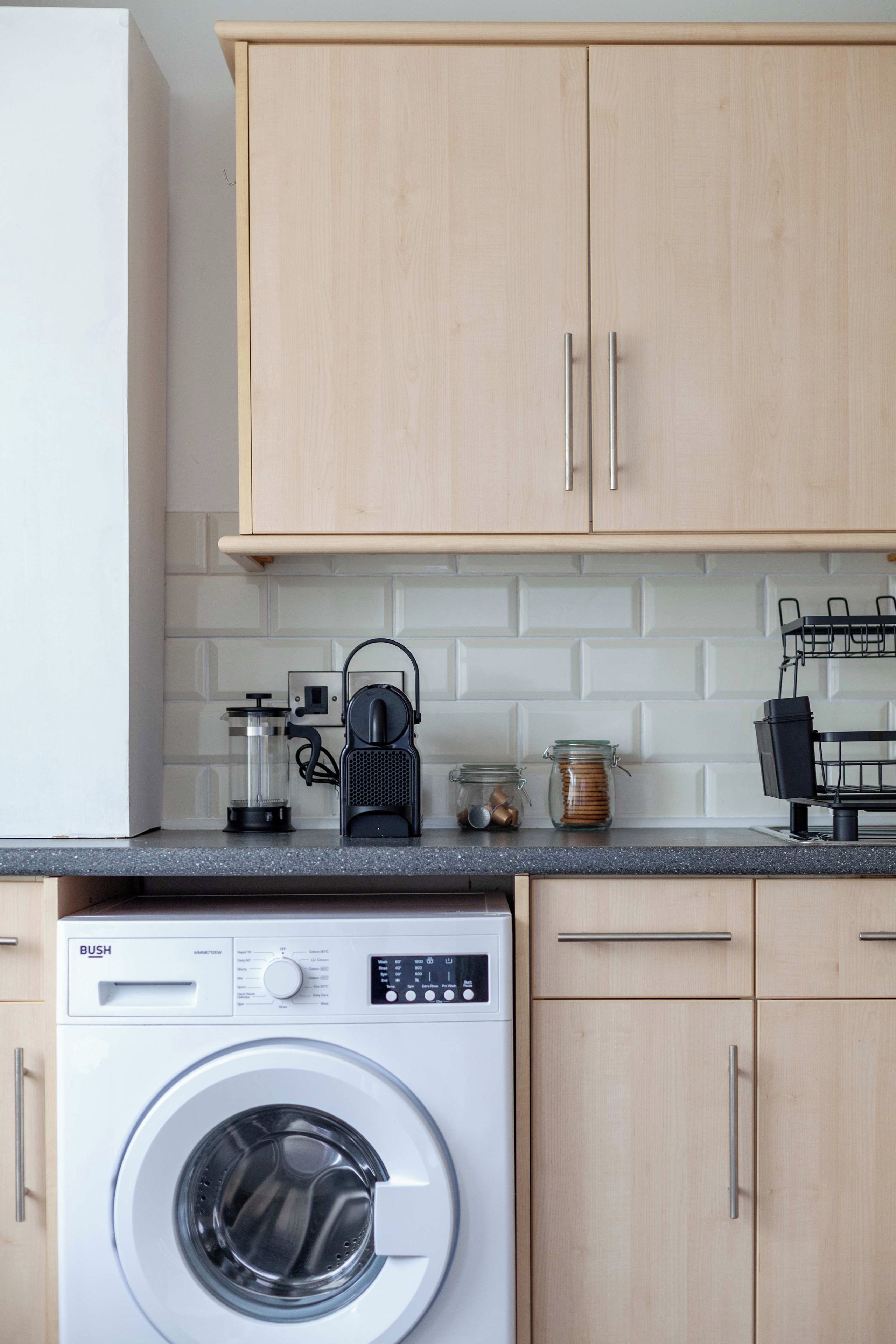 Una cocina con lavadora, armarios de madera y una encimera con diversos objetos.