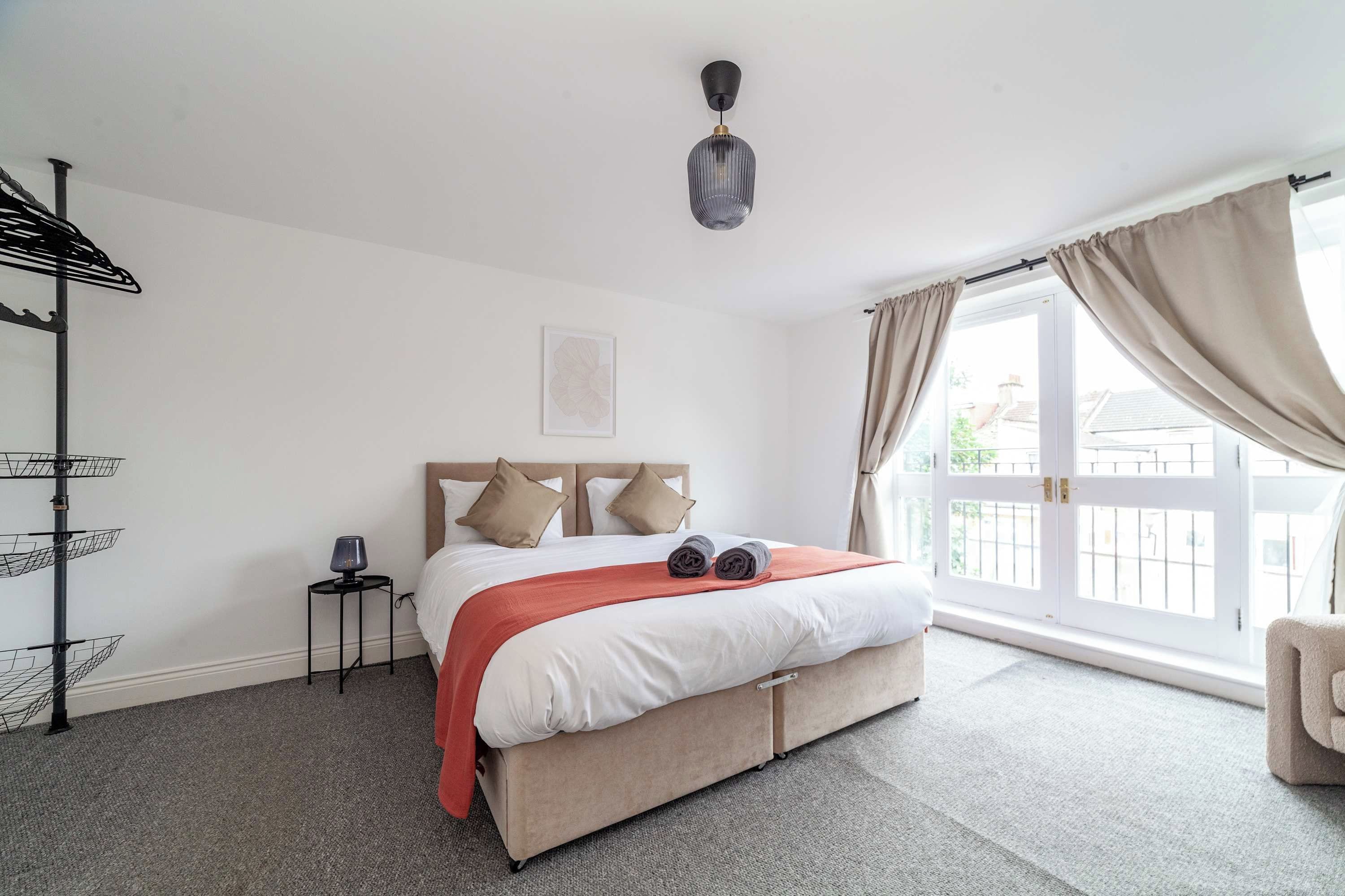 A hotel room with a bed, a side table, a lamp, a window with curtains, and a view of the outside.