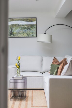 A modern living room with a white sofa, a black metal coffee table, a vase with yellow flowers, and a painting on the wall. - Gorgeous 3 bed flat, Kilburn - Central Location (Greater London)