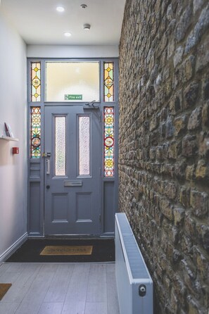 A grey door with a fire exit sign, a doormat, and a stone wall. - Gorgeous 3 bed flat, Kilburn - Central Location (Greater London)