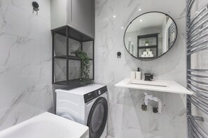 Ein modernes Badezimmer mit Waschmaschine, rundem Spiegel und weißem Waschbecken.