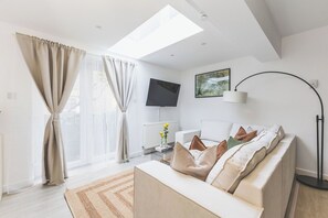 Ein modernes Wohnzimmer mit einer Couch, einem Flachbildfernseher, einer Stehlampe und einem Bild an der Wand.