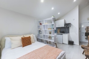 Ein Schlafzimmer mit einem Bett, einer weißen Regalkonstruktion, einer Küchenzeile und einem Sessel.