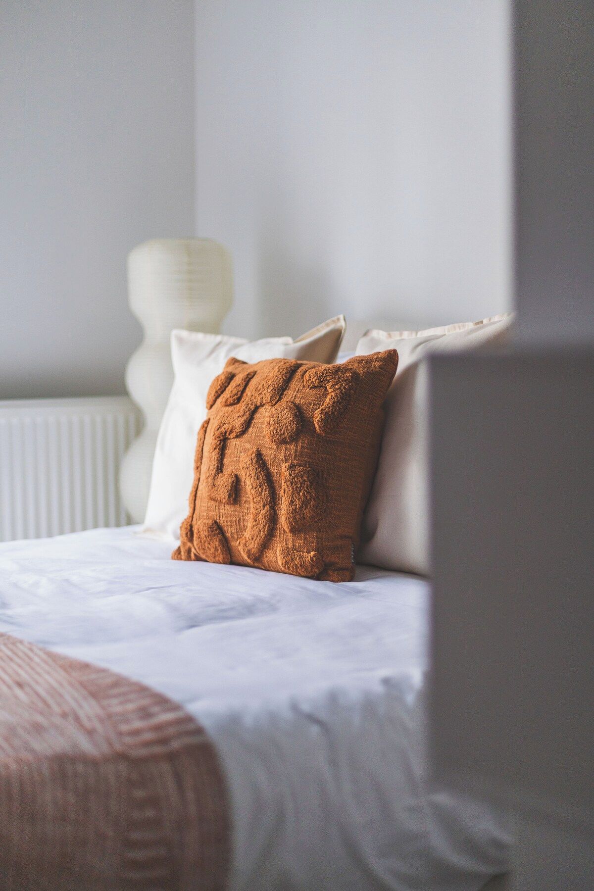 Een bed met witte lakens en een bruin kussen met structuur.