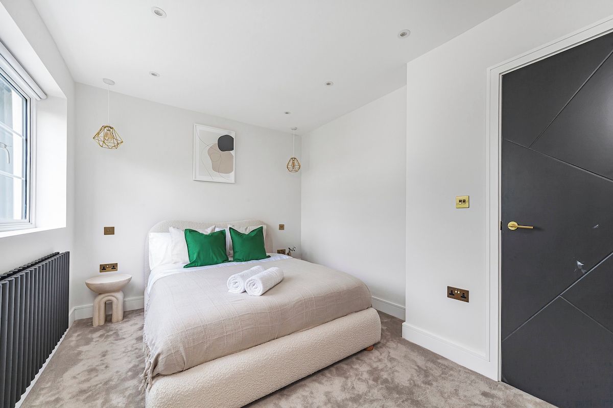 Un dormitorio con cama, mesitas de noche, un radiador, una ventana y una puerta.