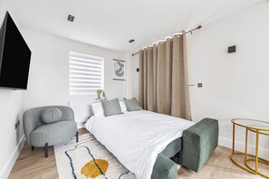 A modern bedroom with a bed, a chair, a small table, and a TV mounted on the wall. - Chic and Classy 2BR Penthouse w/ Parking, 6 Guests (Greater London)