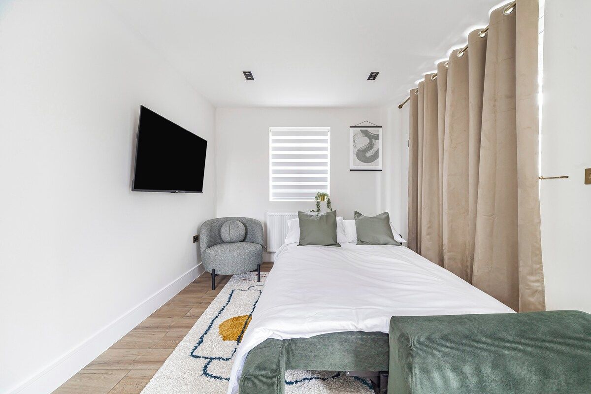 Une chambre à coucher comprenant un lit, une chaise, un téléviseur fixé au mur et une fenêtre avec des stores.