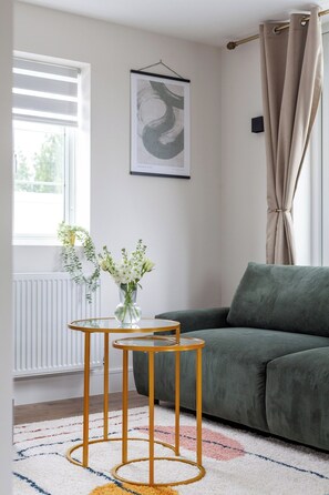 A living room with a green sofa, a glass coffee table with gold legs, and a framed artwork on the wall. - Chic and Classy 2BR Penthouse w/ Parking, 6 Guests (Greater London)