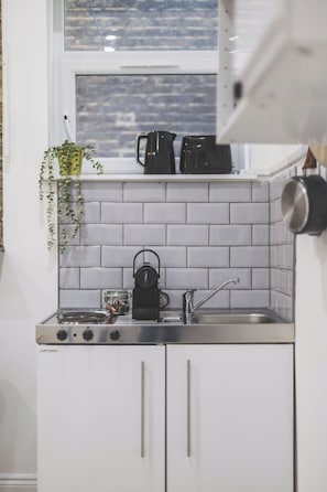 A compact kitchen with white cabinets, a stainless steel sink, a kettle, and a coffee maker. - Stunning studio flat, Kilburn/West Hampstead (Greater London)