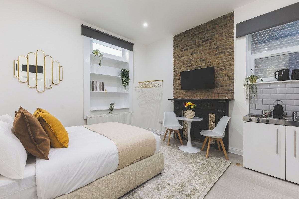 A modern bedroom with a bed, bedside tables, a TV, and a kitchen area with cabinets and a stove.