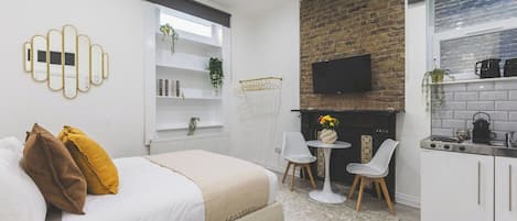 A modern bedroom with a bed, bedside tables, a TV, and a kitchen area with cabinets and a stove.