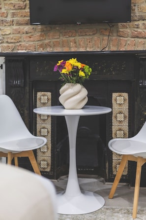 A white table with a vase of flowers, two white chairs, and a fireplace with patterned tiles. - Stunning studio flat, Kilburn/West Hampstead (Greater London)