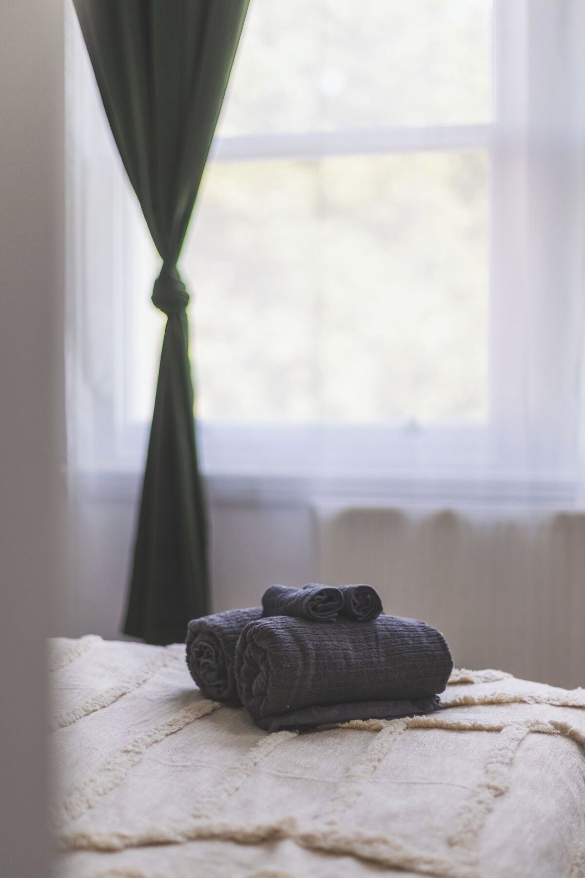 A window with a view of trees, a curtain, and a bed with rolled towels.