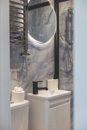 Ein Badezimmer mit Marmorwand, Toilette, Waschbecken mit schwarzem Wasserhahn und Dusche mit Glastür.