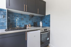Eine Küche mit dunklen Schränken, einem weißen Kühlschrank und einer blaumetallierten Spritzwand.