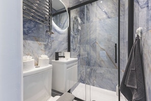 Une salle de bain moderne avec une douche à parois de verre, des carreaux de marbre et un lavabo blanc.