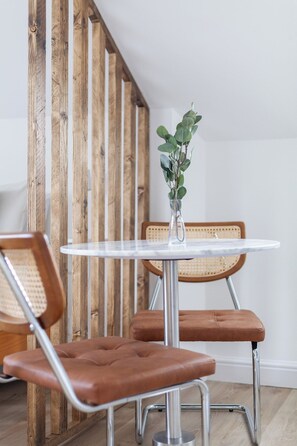 A dining area with a round table, two chairs, a vase with a plant, and a wooden wall. - Modern Studio Flat,Great Location Finsbury Park (Greater London)