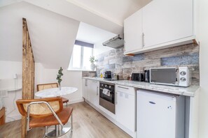 Cocina compacta con armarios blancos, horno empotrado, microondas y refrigerador pequeño.